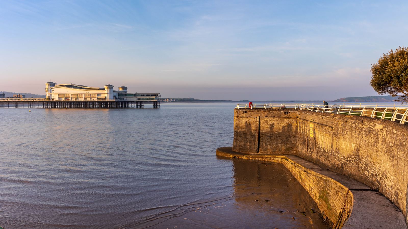 A sunlit harbour wall with the sea and a pier in the background